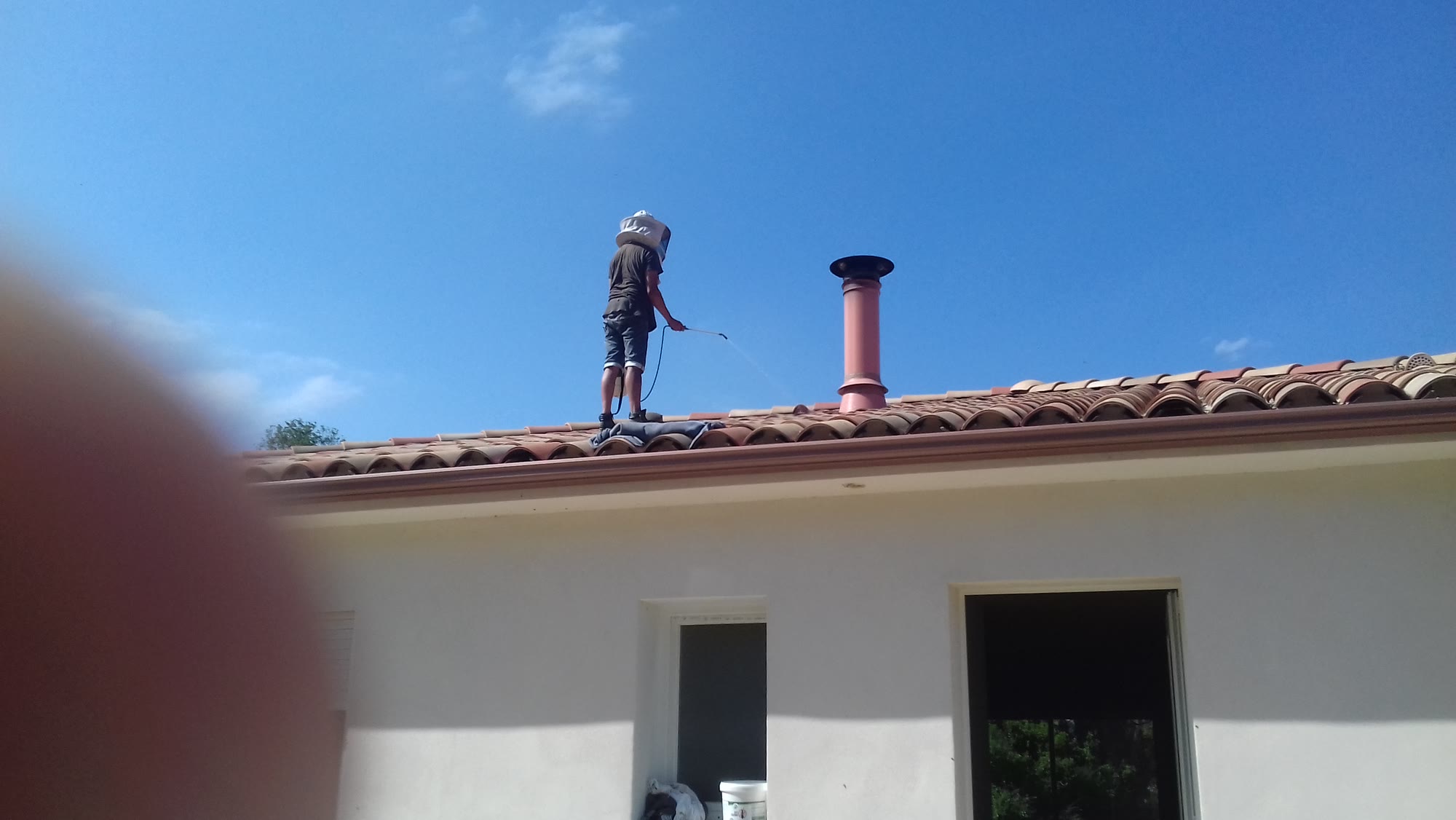 Technicien de Costa Verde Ramonage debout sur la toiture d'une maison, cannes de ramonage à la main, sous un ciel bleu